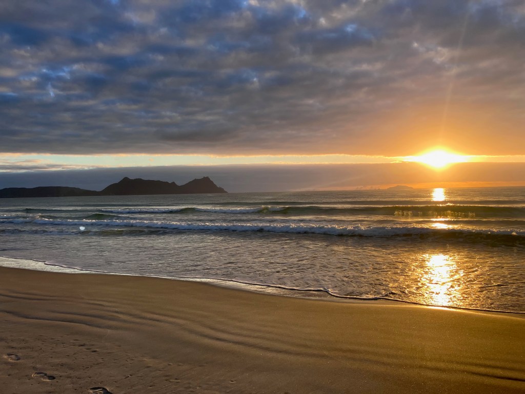photo of an orange sunset through low clouds, reflected in ocean waves on a sandy beach