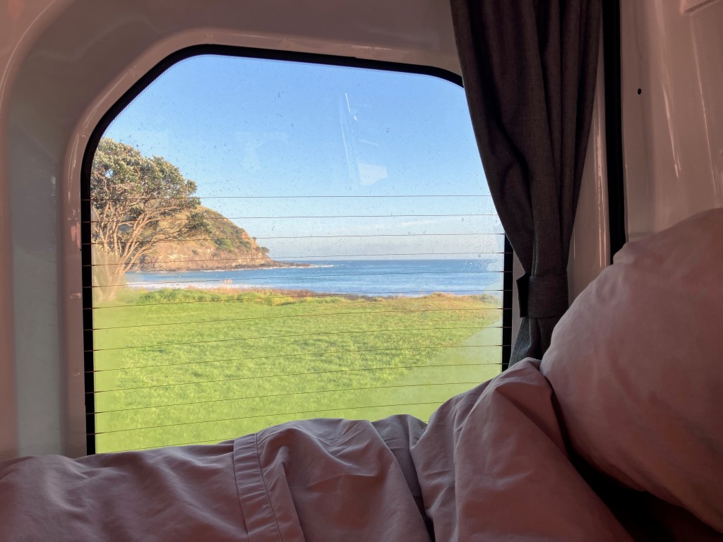 photo looking across a bed through a van window at the ocean