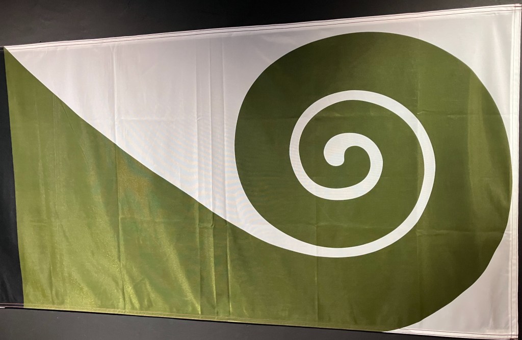 photo of a horizontal flag featuring a green spiral like a young fern or "fiddlehead" on a white background