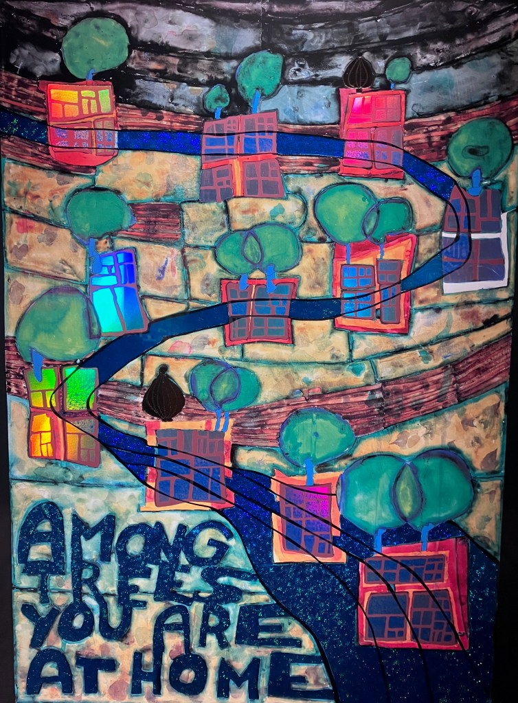 photo of a poster featuring abstract green trees, red squares, a blue path, and the words "AMONG TREES YOU ARE AT HOME"
