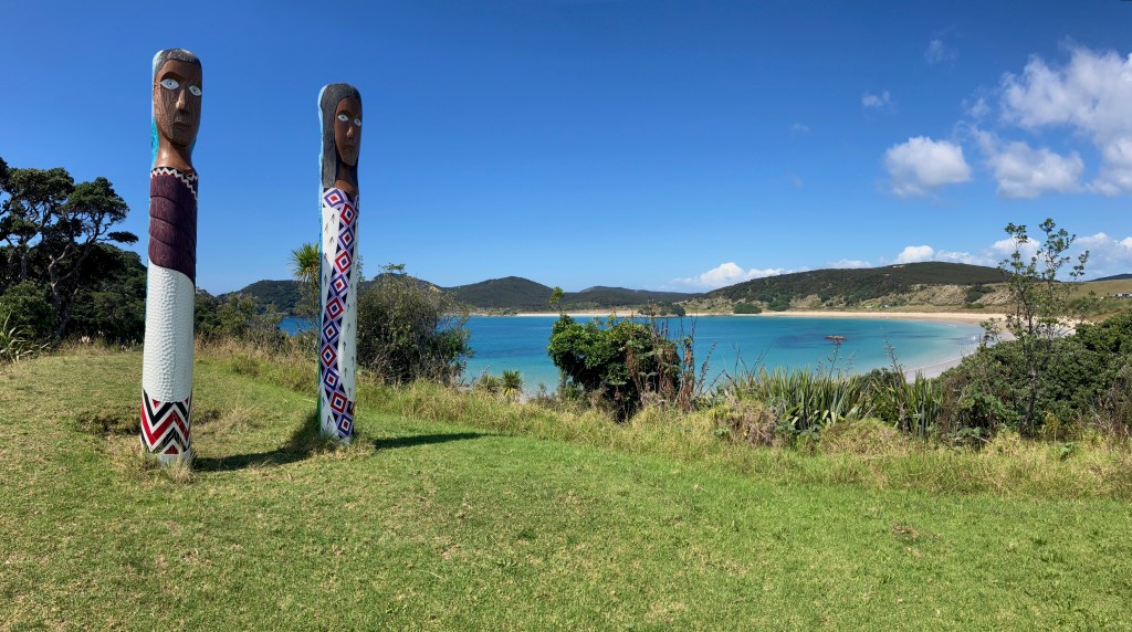 photo of two Maori totem pole sculptures in a field overlooking a beach