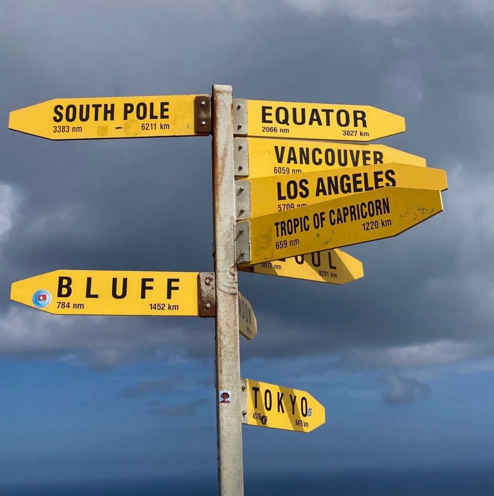 photo of a signpost featuring yellow arrow signs pointing to a variety of destinations, including the South Pole, Equator, Vancouver, Los Angeles, Tokyo, and Bluff (the southernmost point of New Zealand)