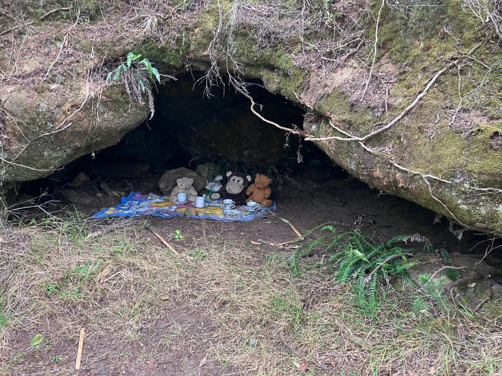 photo of a small cave with stuffed animals inside, sitting on a blanket with a toy tea set on it