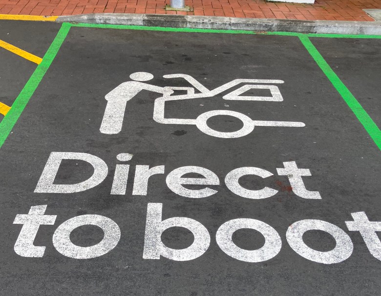 photo of a parking space on black tar with white paint in the image of a person loading a box into the trunk of a car and the words "Direct to boot"