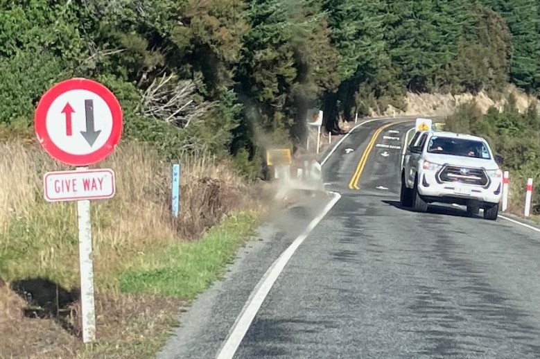 photo of a road with a white pickup truck coming toward us and a sign to the left with a red circle around a small red arrow pointing up and a big black arrow pointing down, with the words GIVE WAY
