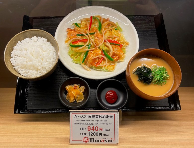 photo of five plates on a black tray tilted vertically, with each dish holding realistic plastic food such as white rice, squash soup, and a noodle dish.