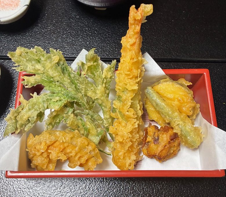 photo of golden brown fried food on a red tray with white paper underneath, including a jagged green leaf, a straight pink tube, and three undefinable scrunchy pieces